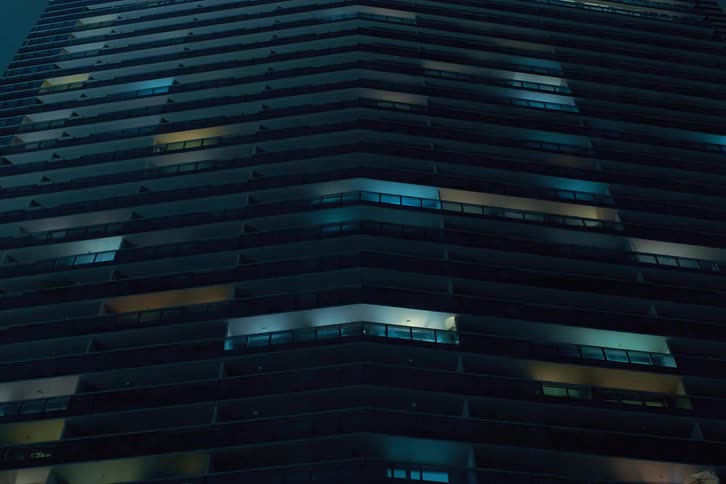 The exterior of modern high rise buildings at night with illuminated windows flashing and flickering