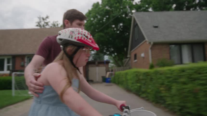 Older brother teaches his younger sister how to ride a bicycle through their residential neighborhood