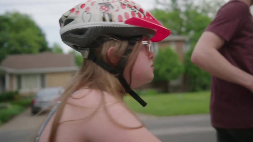 A young girl wearing a helmet learning to ride a bike with her father running next to her