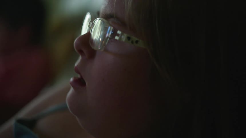 Profile of a young blonde girl wearing glasses while watching television