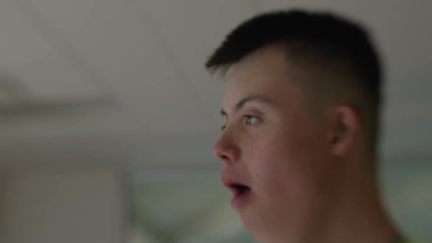 A young man in a gray shirt with yellow details is opening his mouth and closing it