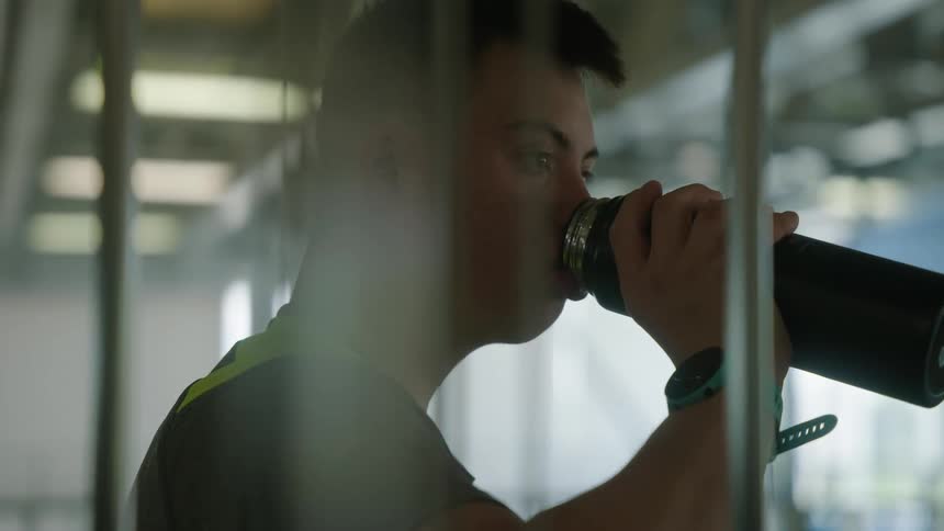 A young boy in a gray shirt is drinking something from a black bottle