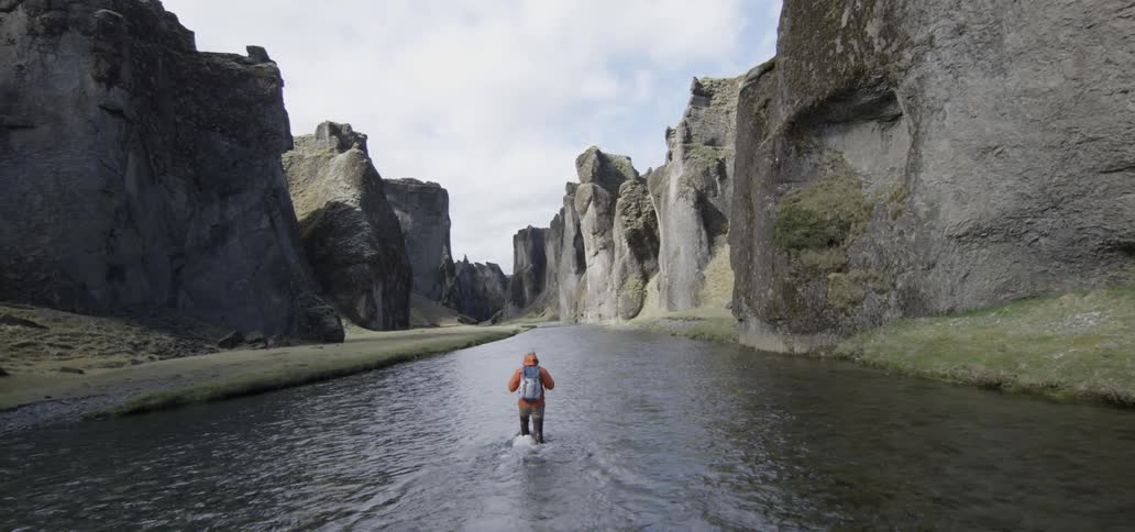 A man walking in a large stream of water between mountains