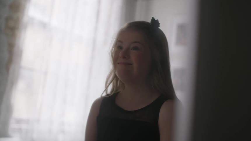 Blonde teenage girl standing alone in a room smiles