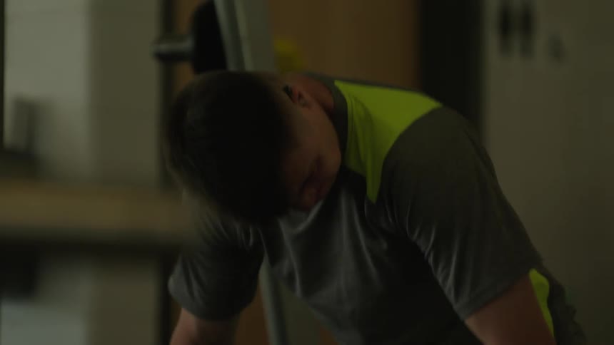 A person wearing a gray tshirt with reflective yellow stripes lifting weights at the gym