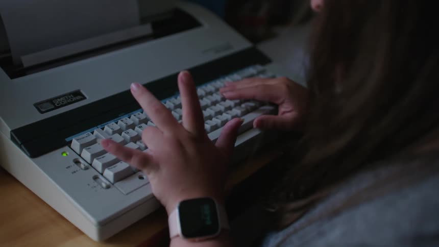 Close up of a young girl wearing a smart watch typing on a keyboard at her desk