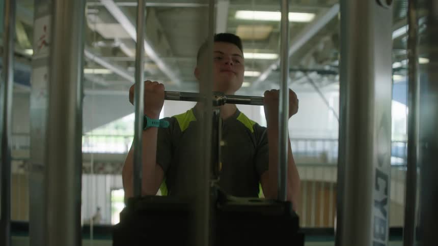 A young male teen lifting a weight bar determined