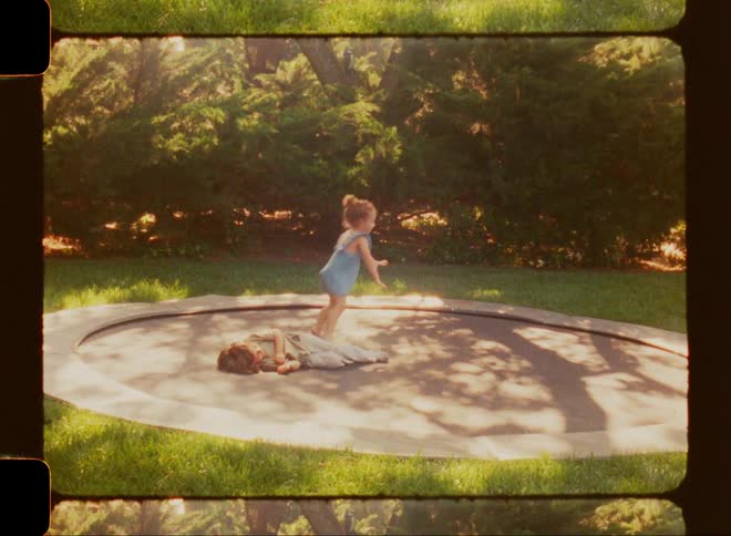 A young boy and girl jumping around on a trampoline in their backyard in the summer