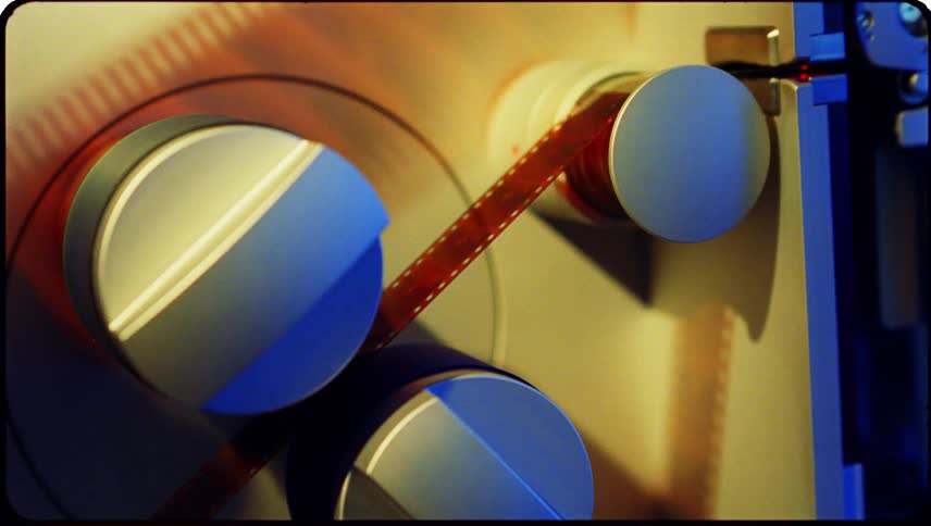 Up close of film sliding through rotators on a machine casting shadows on the machine