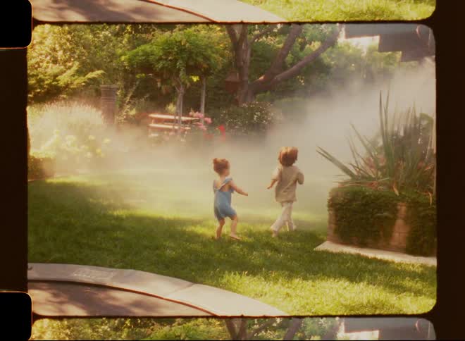 Two children playfully run through a mist of water in the backyard