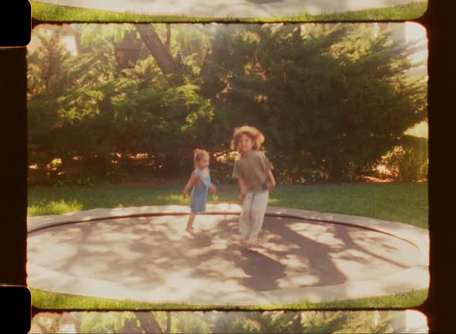 A little girl and boy jumping on a trampoline in the middle of a summer day in their backyard