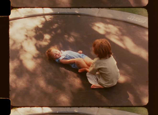 A young boy and girl playing and laughing on a trampoline in the sun
