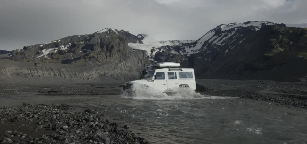 White suv rolling through some shallow moving water on a very cloudy day