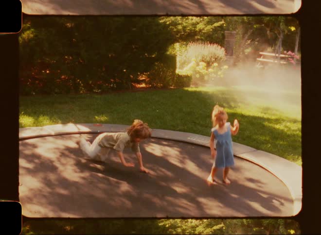 A young boy and girl jumping on a trampoline in their backyard in the summer
