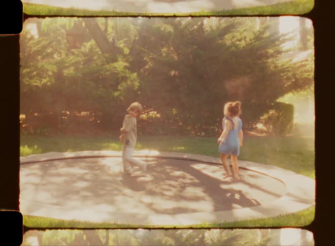 Two children jumping on a trampoline on a sunny day in the backyard