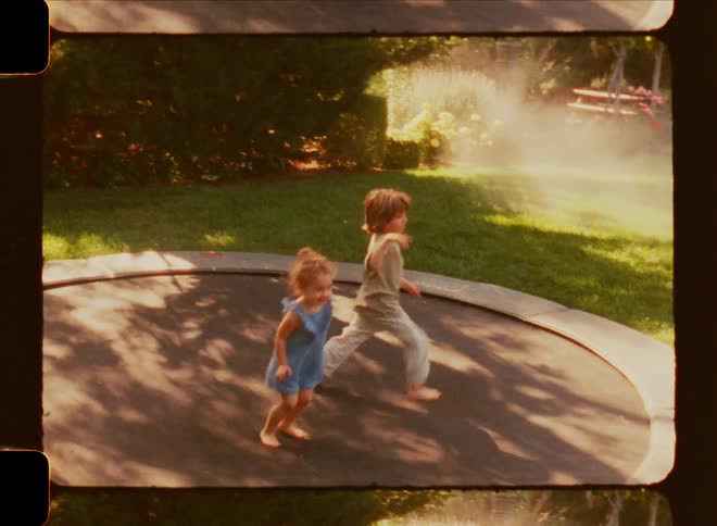 A young brother and sister jumping on a trampoline on a bright sunny summer day in their backyard