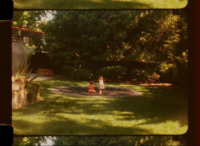 Children playing on a trampoline set into the grass in the backyard