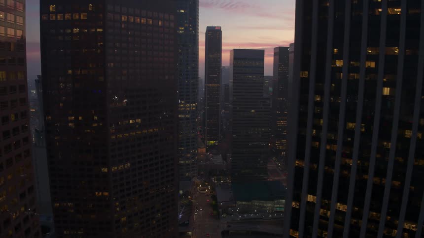 City skyscrapers with lights on in the buildings and the sun setting on the horizon