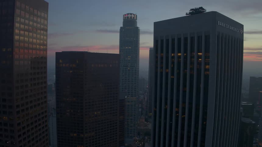 Epic aerial appraoching downtown city buildings at dusk with some office lights on in the windows