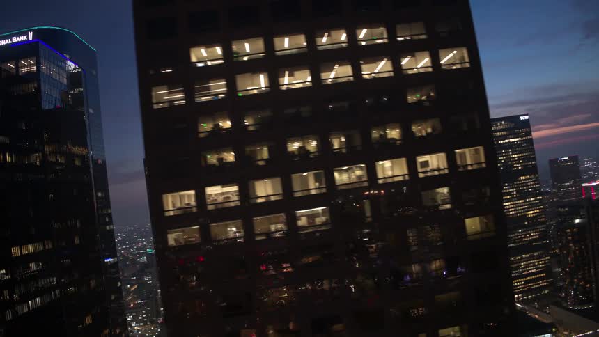 Arching aerial of reflective city office buildings lit up at night over a dense downtown city skyline