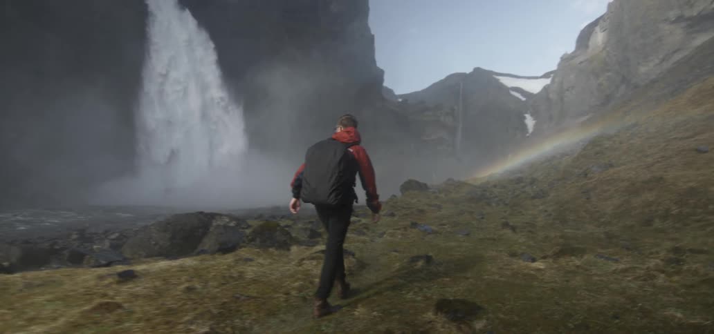A hiker walks near a large waterfall