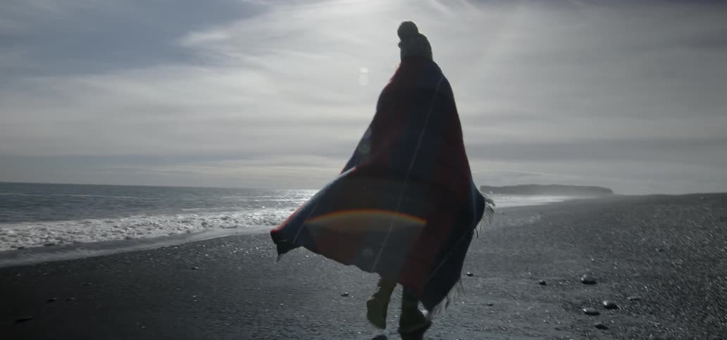 A woman walking along shore on a beach on a cloudy afternoon