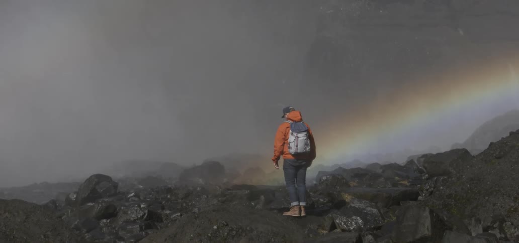 Man hikes up a mountain with a rainbow in the sky
