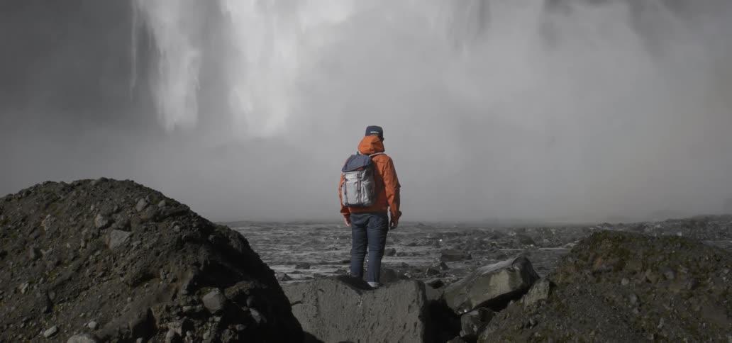 A man stands at the bottom of a waterfall