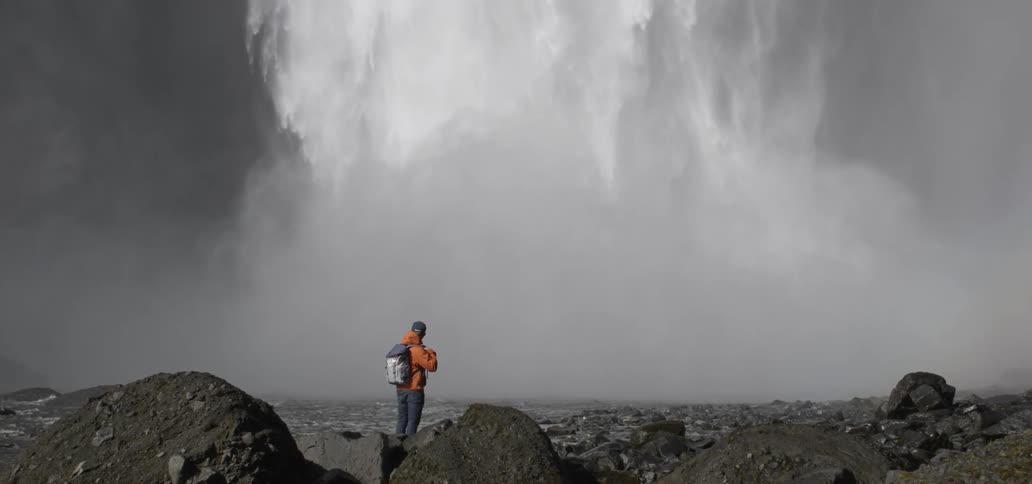 A person stands watching the water plunge over a cliff