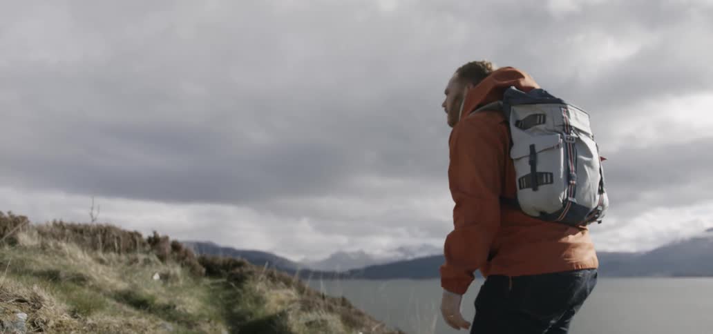 A hiker walks up a grassy hill near a lake