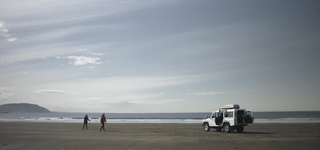 Two people standing on the shoreline before walking back towards their vehicle