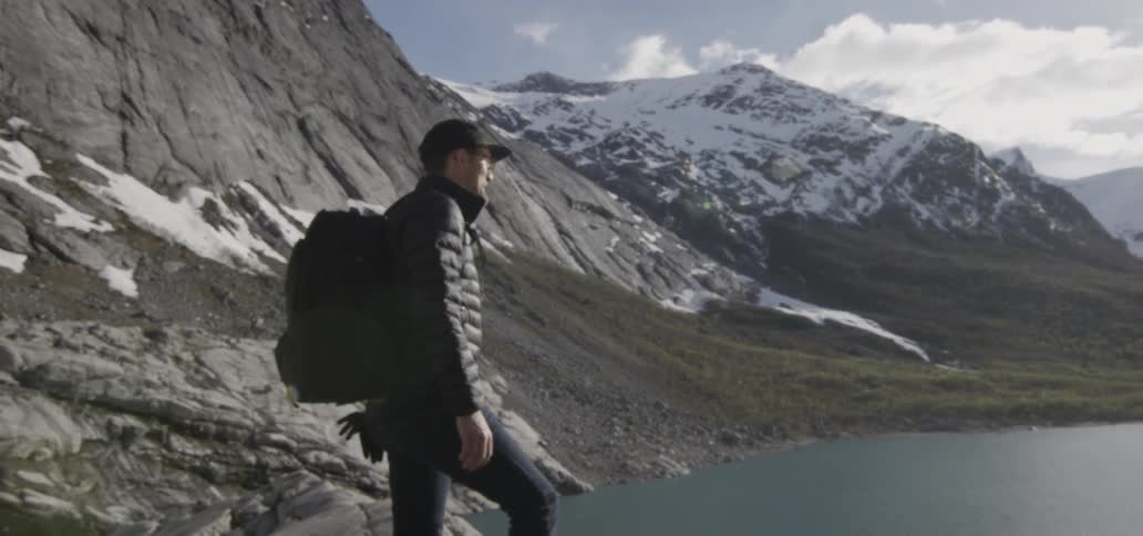 A man with a backpack is standing next to a mountain looking around