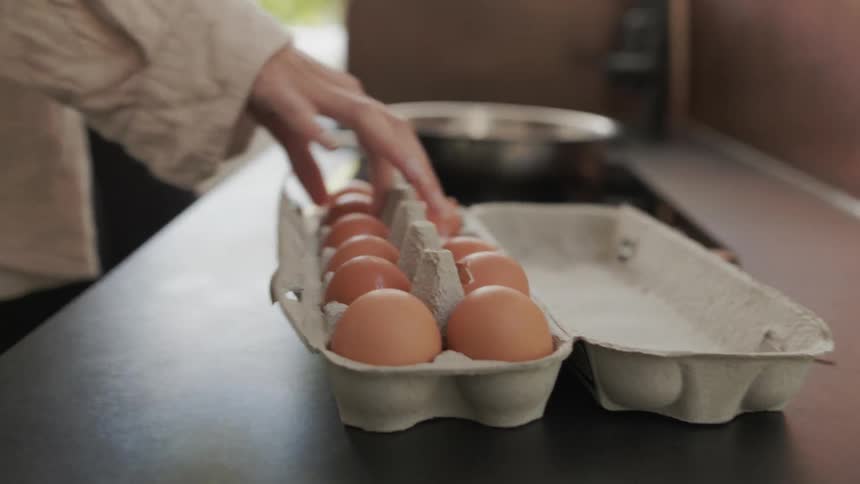 A person opens an egg carton and removes an egg from it on a kitchen counter