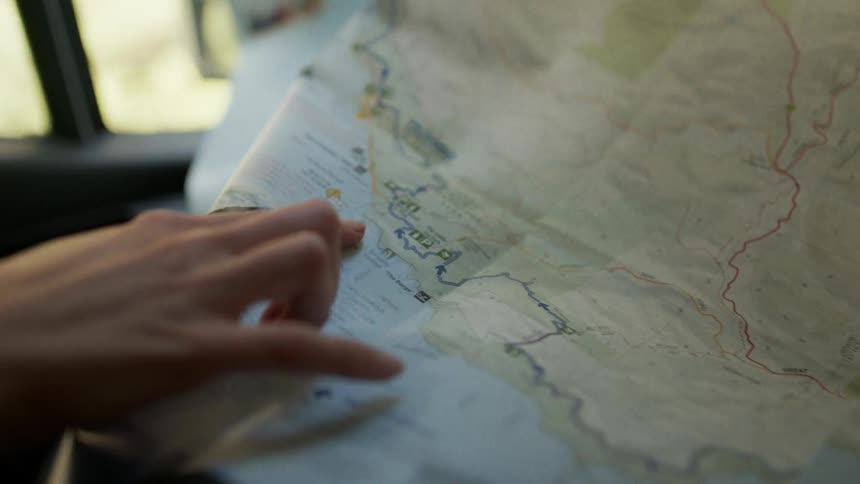A persons finger pointing to a map on a piece of paper near a window