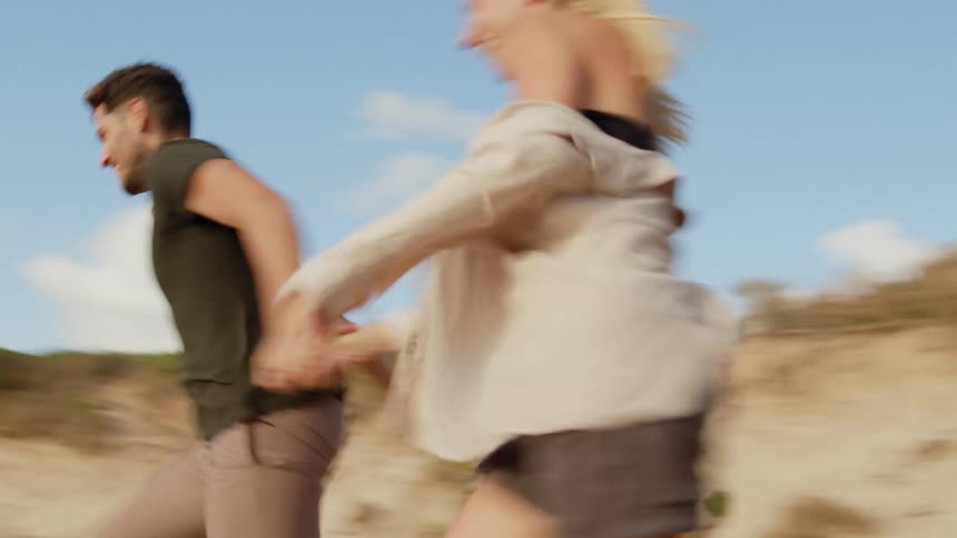 A man and a woman hold hands while running down stairs leading to a beach