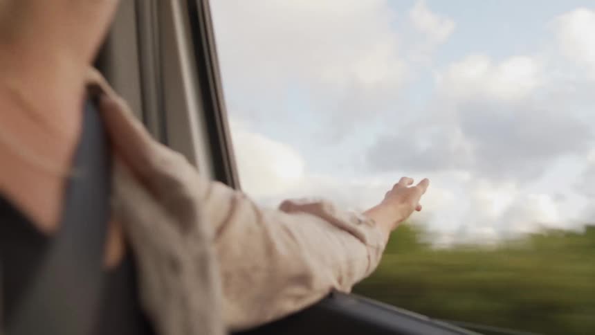 A clip of a ladys hand out of the window of a moving vehicle