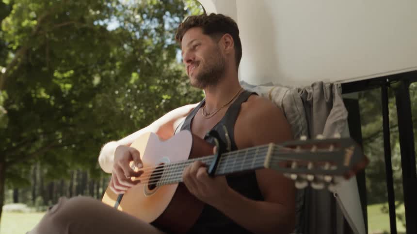 Man plays a guitar while camping near the woods on a summer day