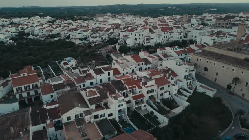 Red roofed buildings fill a residential area near multiple groves of trees and a large building with a courtyard on a hazy day