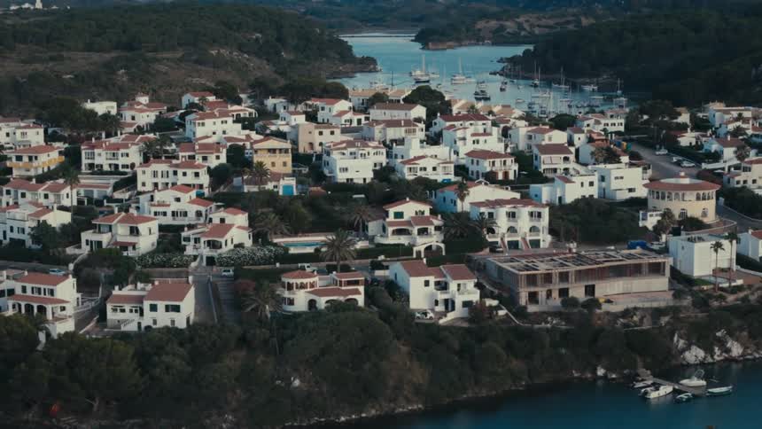 Boats line the river passing by a residential area surrounded by forest on a misty day