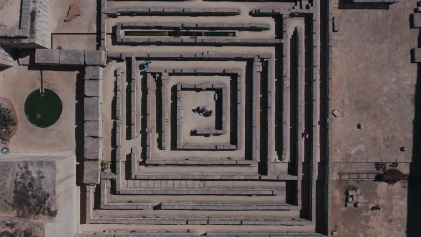 An aerial view of a stone maze with people moving around in the center