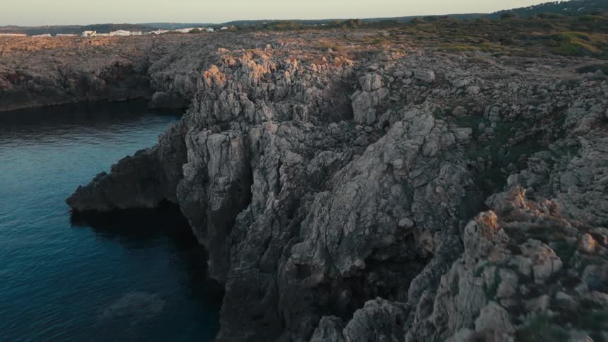 Waves flow toward the base of craggy cliffs at the edge of a rocky plain on an overcast day