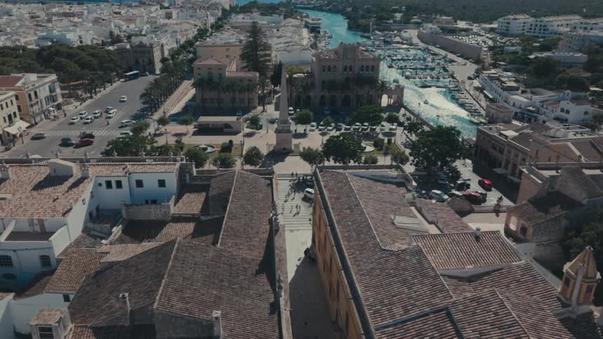 Aerial of city building rooftops and a monument in the middle of a city square on a bright sunny day