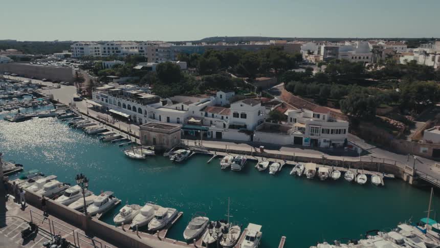 An aerial view of a harbor town with boats docked in a canal and people walking along the waterfront