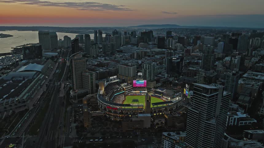 An aerial view of a baseball stadium in a downtown cityscape at dusk