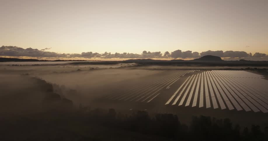 Dense fog partially obscures the solar panels on a solar farm as red tints the horizon