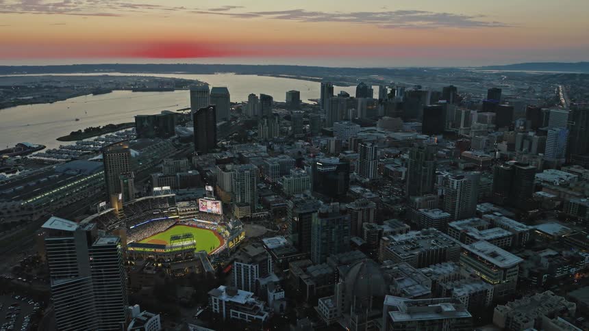 An aerial view of a metropolitan city with huge buildings and a brightly lit stadium with a green lawn