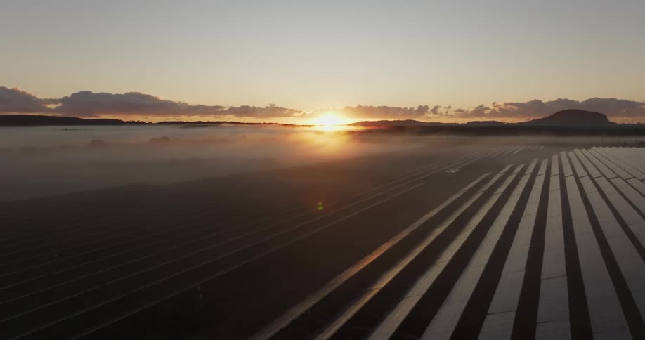A farm of solar panels facing the sun that is rising over the mountains on a clear morning