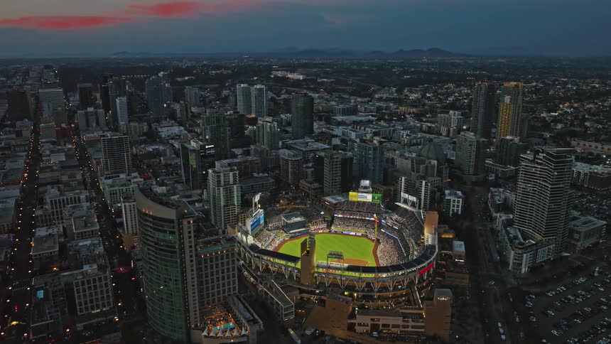 The camera orbits around Petco Park at blue hour sunset as a plane flies by in the background