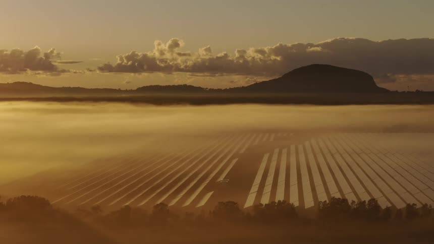 A solar panel farm on a morning with fog hanging over the site
