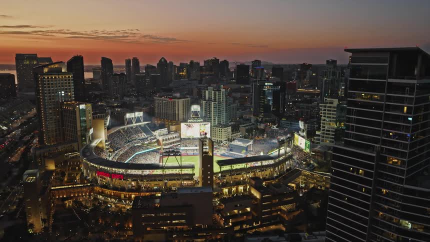 Baseball fans fill brightly lit Petco Park stadium as the camera reveals the waterfront in San Diego at dusk magic hour